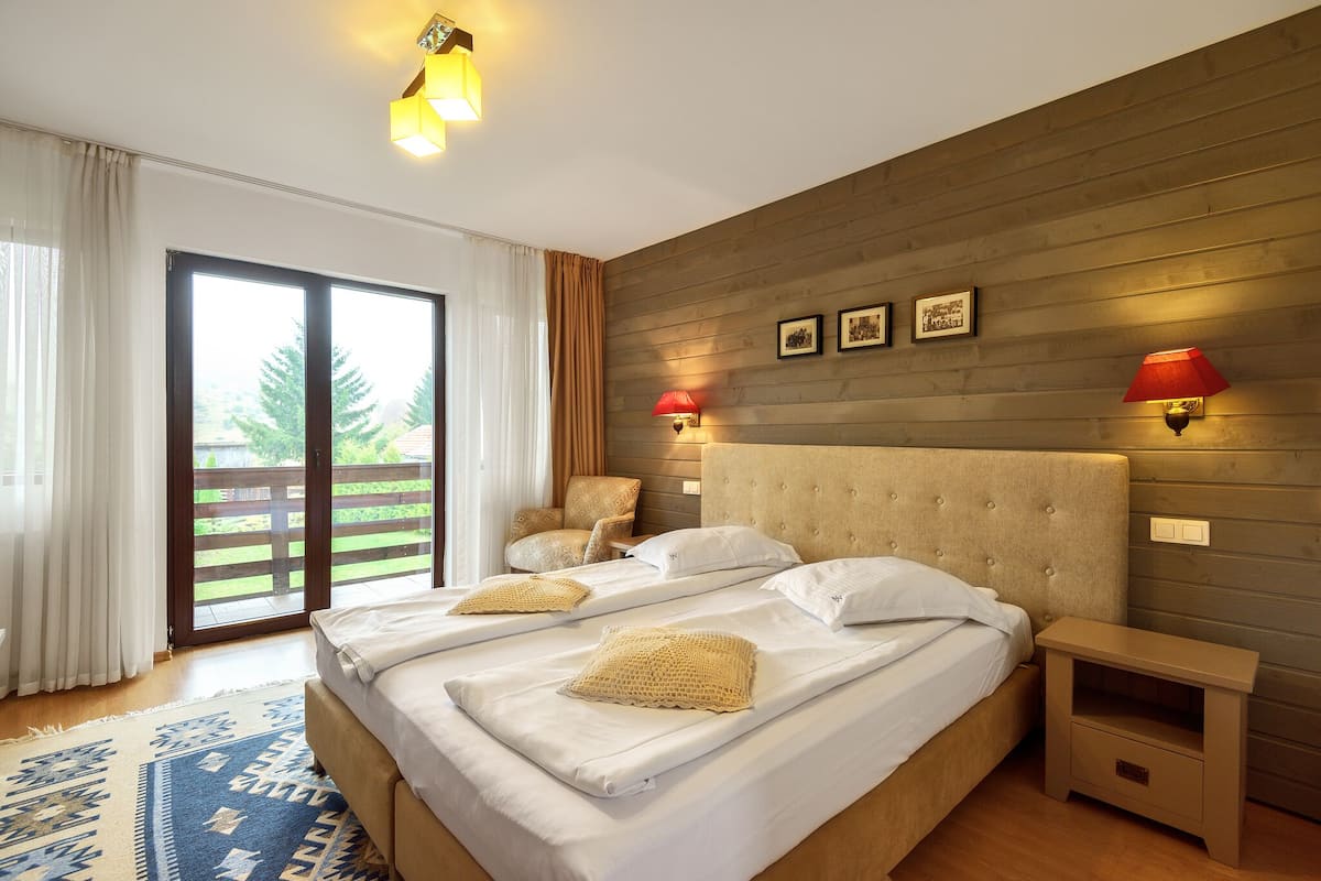 Un dormitorio con una cama grande, dos mesitas de noche, un cabecero de madera y vistas al exterior a través de una puerta corredera.
