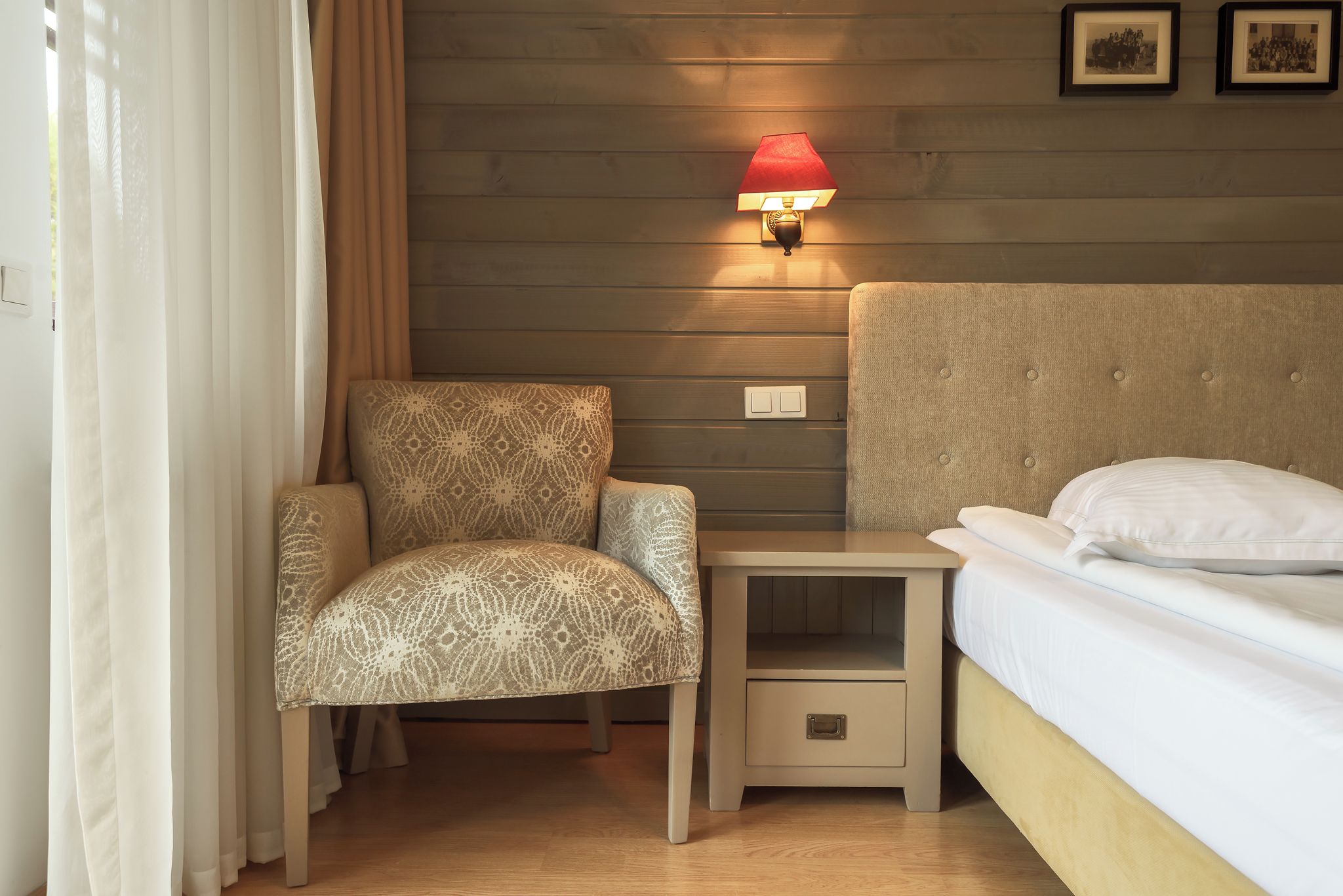 Habitación de hotel con cama, mesita de noche, silla y lámpara de pared.