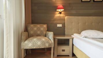 Habitación de hotel con cama, mesita de noche, silla y lámpara de pared.