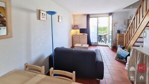 Una habitación con sofá, mesa de comedor, sillas, lámpara, armario y vistas al exterior.