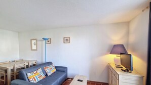 Una sala pequeña con sofá, televisión, lámpara y mesa de comedor.