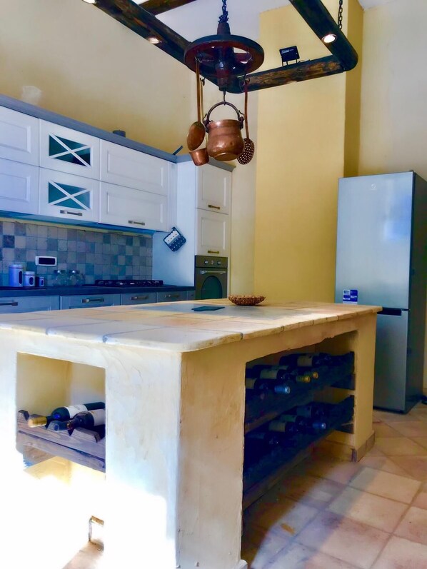 A kitchen with white cabinets, a central island with wine storage, a hanging copper pot, and a modern refrigerator.