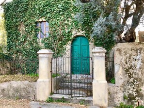 A green door with a wrought iron gate, flanked by two stone pillars, set against a wall partially covered in ivy.