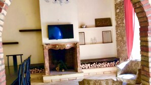 Een woonkamer met een open haard, een televisie en een eetgedeelte met stoelen.