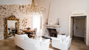 A living room with a stone wall, a fireplace, a chandelier, and white furniture.