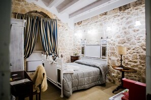 Ein Schlafzimmer mit Stehwand, einem Bett mit grauer Bettdecke, einem Nachttisch mit Lampe und einem kleinen Tisch mit Stuhl.