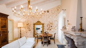 A cozy living room with a stone wall, a chandelier, a fireplace, and a dining area.