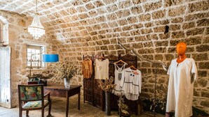 A rustic room with stone walls, a wooden table, a chair, and a mannequin displaying clothing.