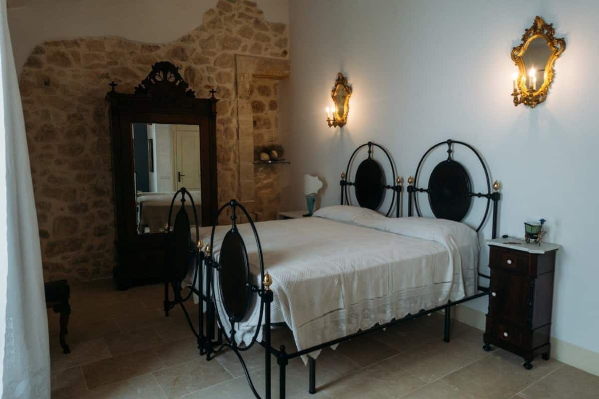 Ein Schlafzimmer mit Steinwand, einem Bett mit Metallgestell, einer Holzkommode und zwei Wandleuchten.