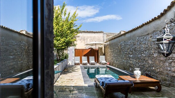 A courtyard with a pool, lounge chairs, and a wooden table.