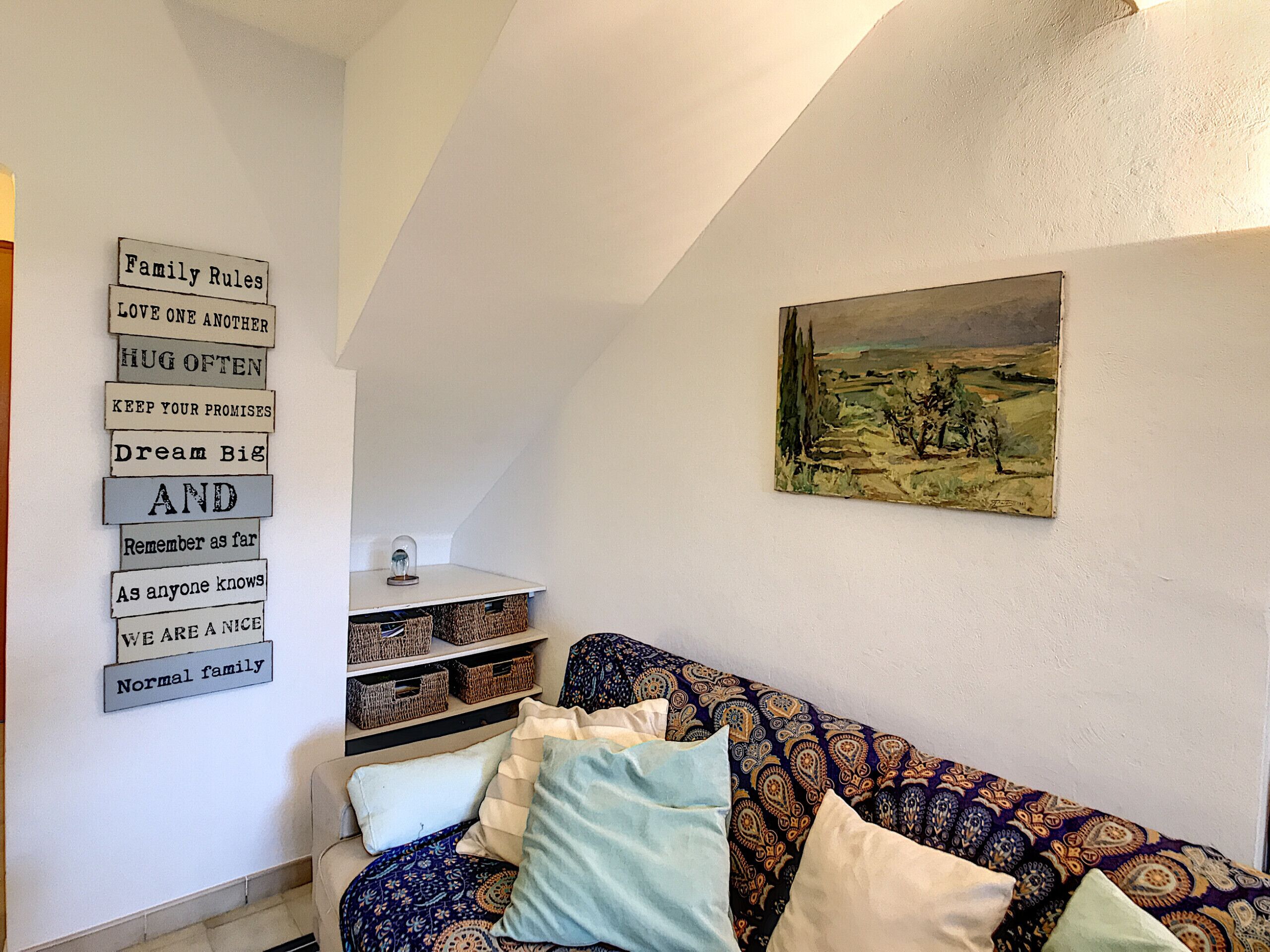 Een gezellige woonkamer met een gestreept sofa, een wandplank met manden, en een landschap in een lijst.