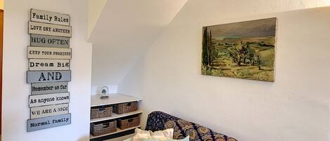 Un accogliente soggiorno con un divano decorato, uno scaffale a parete con cesti e un quadro raffigurante un paesaggio.