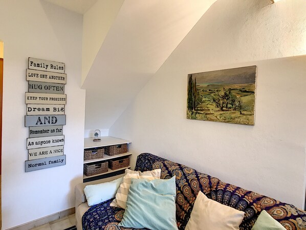 Ein gemütliches Wohnzimmer mit einem gemusterten Sofa, einem an der Wand befestigten Regal mit Körben und einem gerahmten Landschaftsbild.