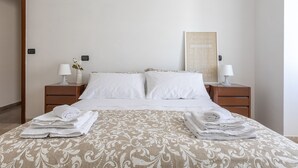 A neatly made bed with a patterned bedspread, two white pillows, and two bedside tables with lamps and a vase of flowers. - Comfort House 14 (Roseto degli Abruzzi)