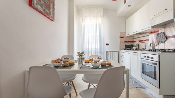A modern kitchen with white cabinets, a dining table with chairs, and a breakfast setting. - Comfort House 14 (Roseto degli Abruzzi)