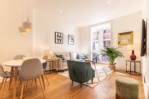 A modern living room with a dining area, a sofa, a green armchair, a coffee table, and a potted plant.