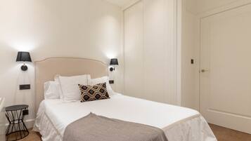 Un dormitorio ordenado con cama, dos lámparas de noche, una mesita de noche y una puerta.