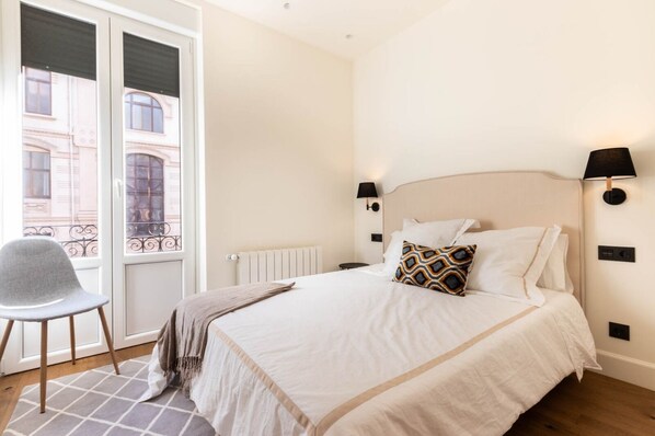 A hotel room with a bed, a chair, a window, and a radiator.