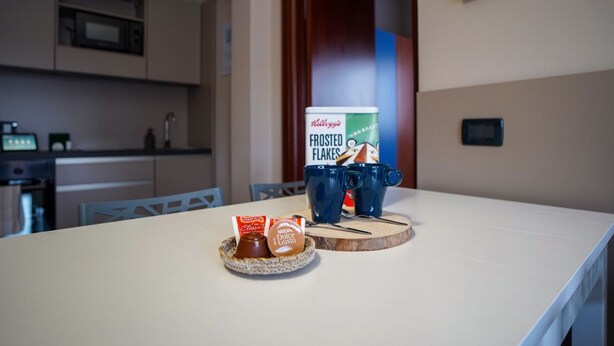 A kitchen with a microwave, toaster, and coffee maker. There is a box of Kellogg's Frosted Flakes and two mugs on the counter. - 2 bedroom apartment-Expo Residence Rho (RHO)