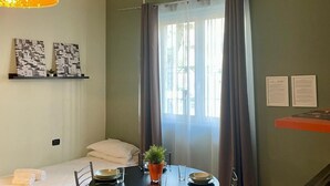 A hotel room with a bed, a dining table with chairs, a potted plant, and a window with curtains. - Bilocale Residence La Red R1 (RHO)