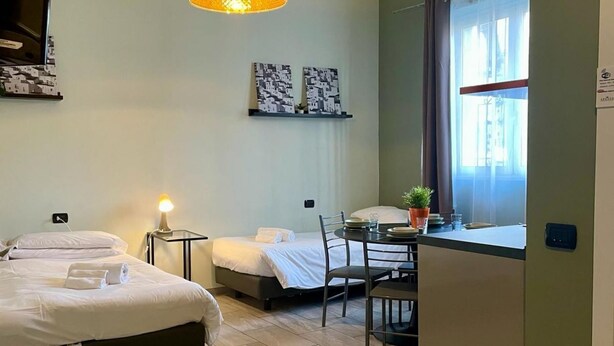A hotel room with two beds, a dining table, chairs, a small potted plant, and artwork on the wall. - Bilocale Residence La Red R1 (RHO)