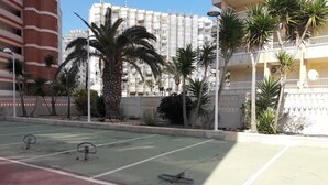 Ein Tennisplatz im Freien mit einer Palme und einem Hotel im Hintergrund.