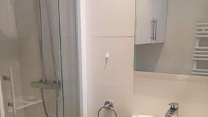 Een moderne badkamer met een douchecabine van glas, een wit wastafelmeubel met zeepbakje en een spiegel erboven.