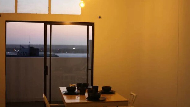 Uma varanda com mesa posta para refeições, uma cadeira e vista para a cidade.