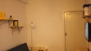 Uma sala de estar com sofá, uma mesinha, luminária e TV fixada na parede.