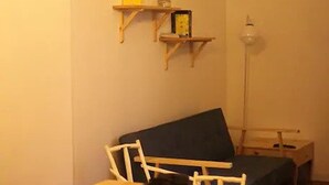 Um quarto aconchegante com uma mesa de madeira posta para chá, uma cama com cobertura azul e uma estante com um relógio e uma caixa amarela.