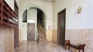 Um corredor com piso de mármore, um banco de madeira, uma escadaria e um aparelho de luz fixado na parede.