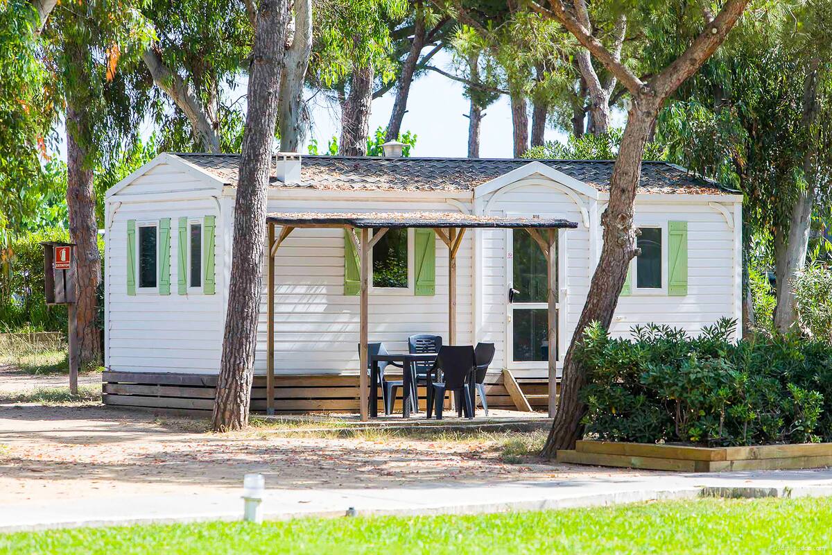 Une petite maison mobile de plain-pied, dotée d’une véranda et d’une table avec des chaises.