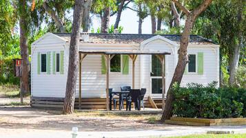 A small, single-story mobile home with a porch and a table with chairs.