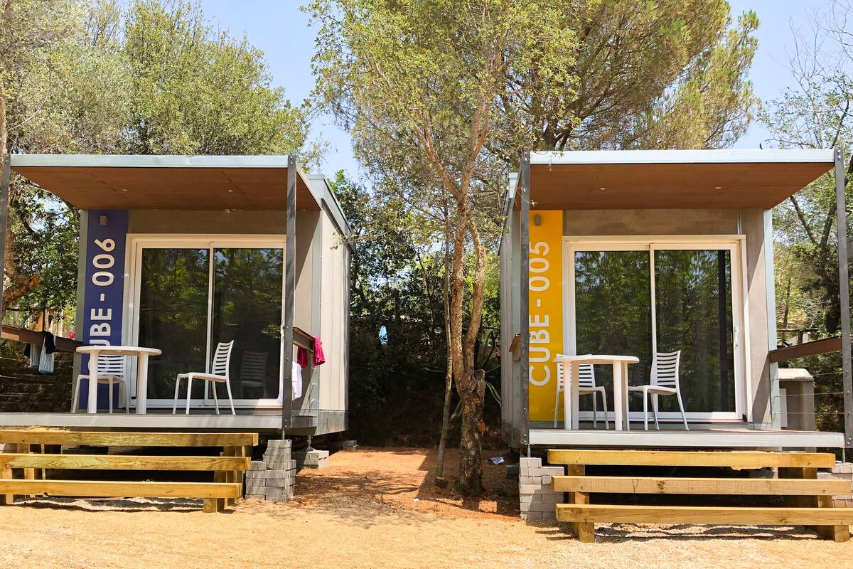 Deux cabanes modernes et minimalistes, dotées de portes et de fenêtres en verre, et comprenant chacune une petite table et un ensemble de chaises.