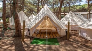 Varias tiendas en forma de cúpula con una zona central para dormir y un ventilador, rodeadas de árboles.