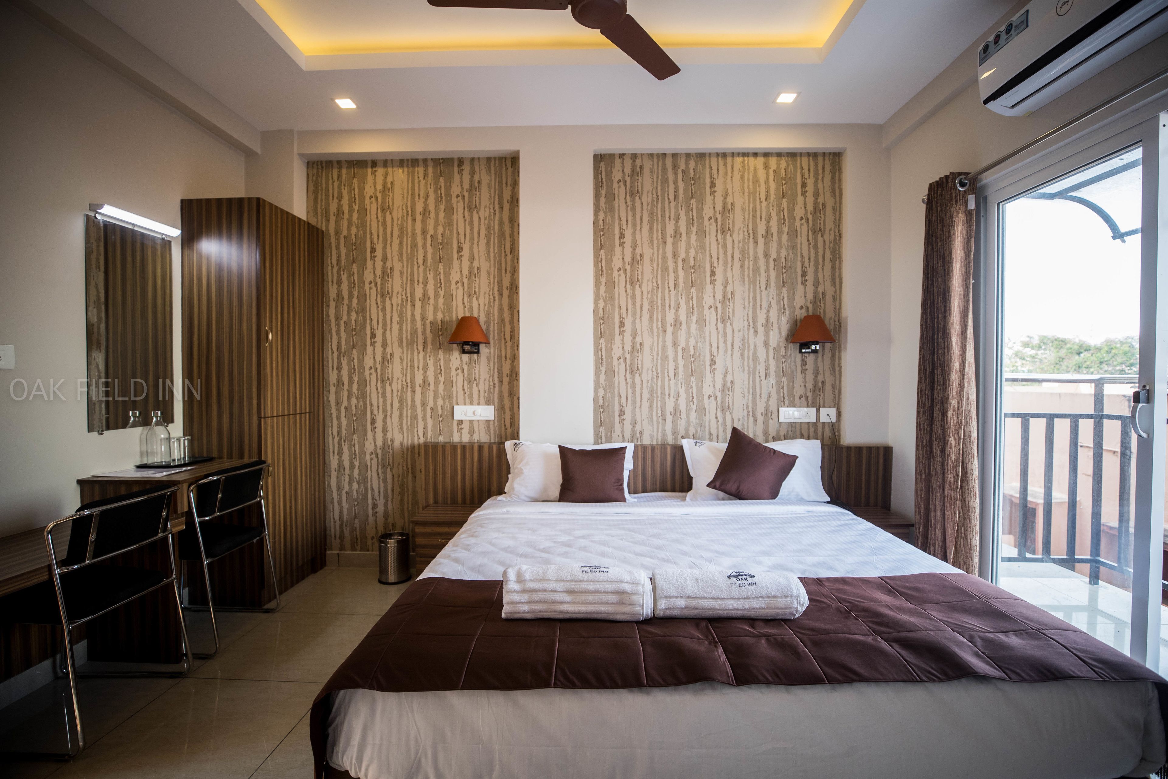A hotel room with a large bed, a desk with chairs, a ceiling fan, and a view of the outdoors.