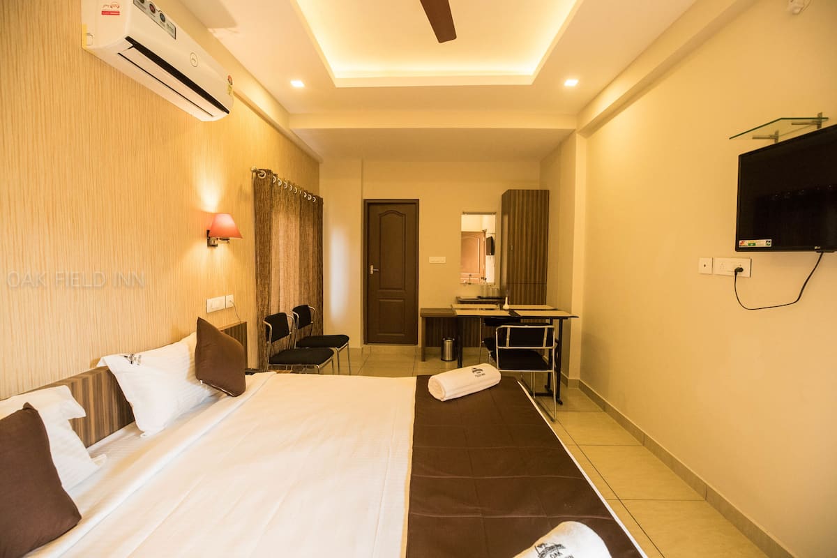 A hotel room with a bed, a desk, a chair, a TV, and an air conditioning unit.