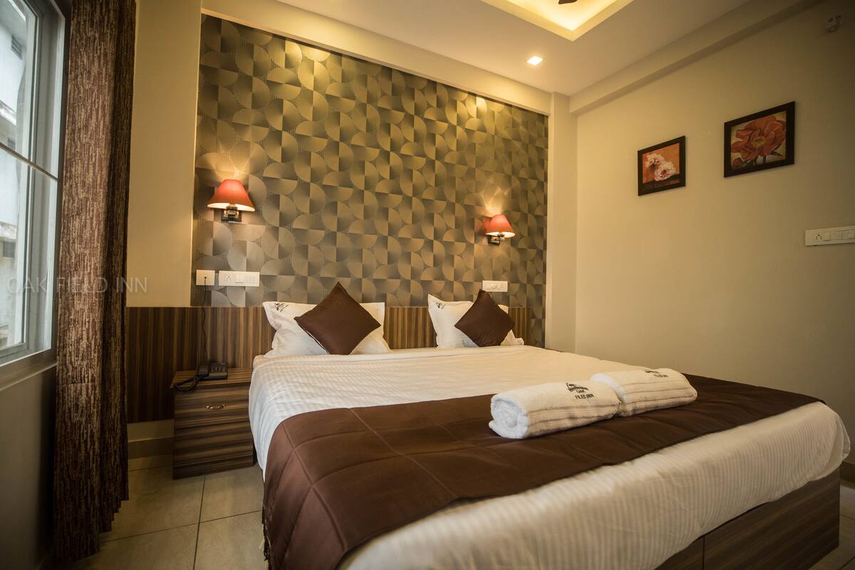 A hotel room with a large bed, two wall-mounted lamps, a window with curtains, and a patterned wall.