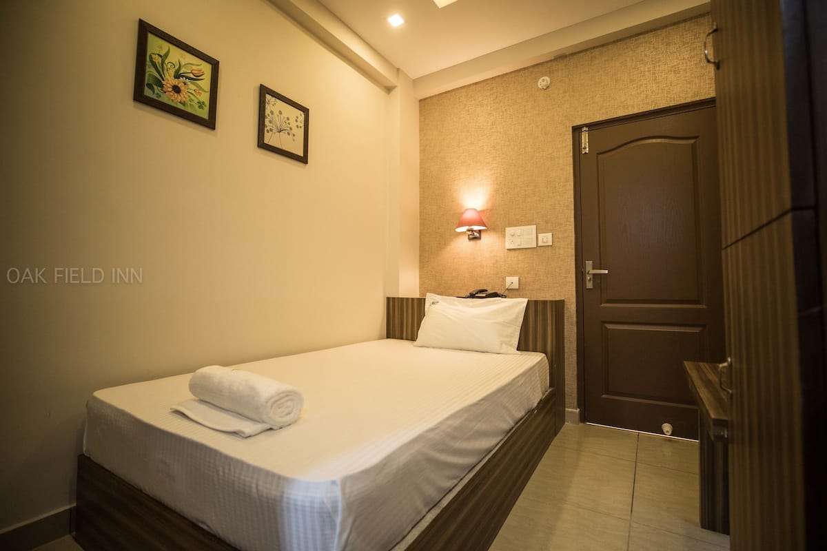 A neatly made bed with a rolled towel, a wall-mounted lamp, and two framed pictures on the wall.