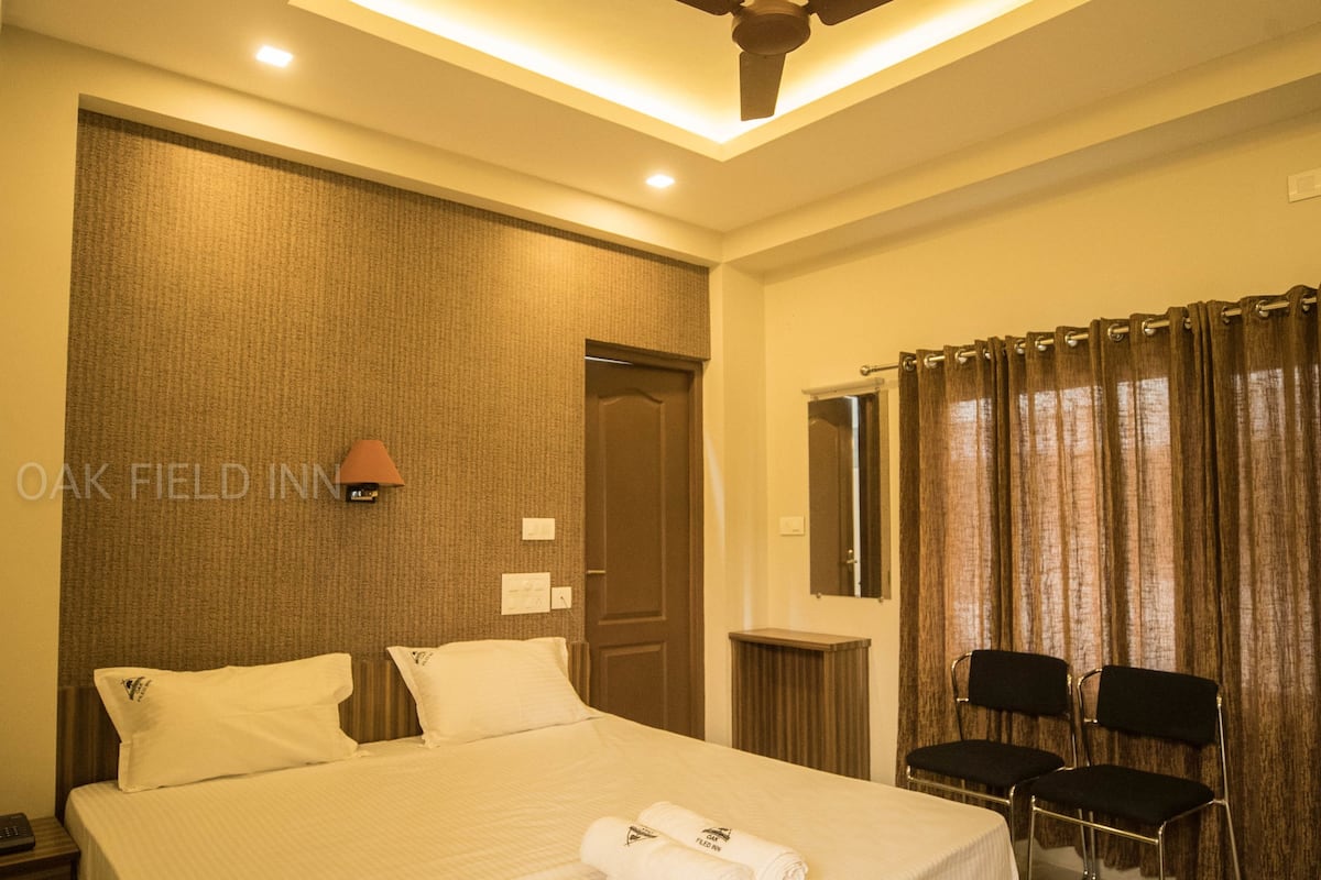 A hotel room with a large bed, a ceiling fan, a desk with two chairs, and a window with curtains.