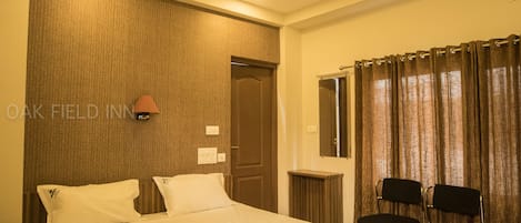 Habitación de hotel con una cama grande, ventilador de techo, escritorio con dos sillas y ventana con cortinas.