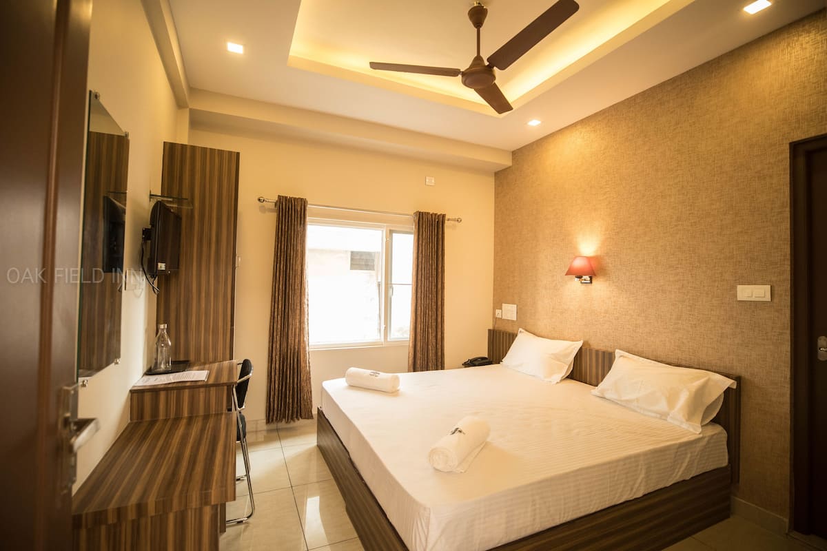 A hotel room with a bed, a desk, a chair, a ceiling fan, and a window with curtains.