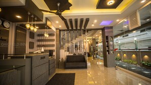 A modern hotel lobby with a reception desk, a sofa, a staircase, and a reception area with a glass partition. - Oak Field Inn (Kanayannur)
