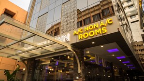 A hotel with a modern glass facade, labeled "A/C NON A/C ROOMS" on the entrance. - Oak Field Inn (Kanayannur)