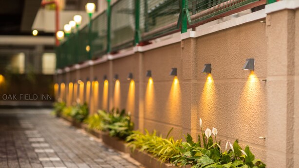 A pathway lined with planters and wall-mounted lights, leading to a building entrance. - Oak Field Inn (Kanayannur)