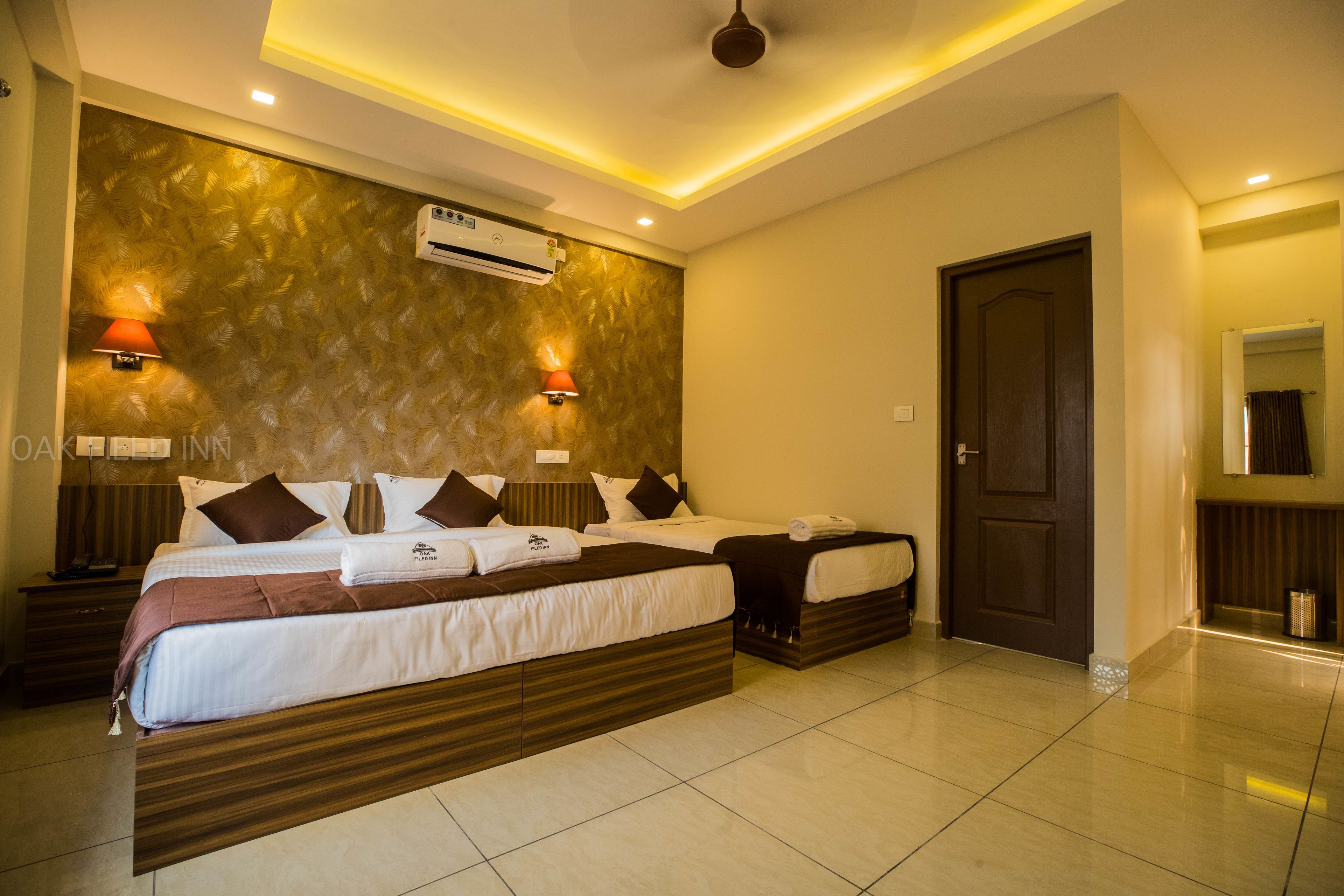 A hotel room with two beds, a large wall-mounted air conditioner, and two wall-mounted lamps.