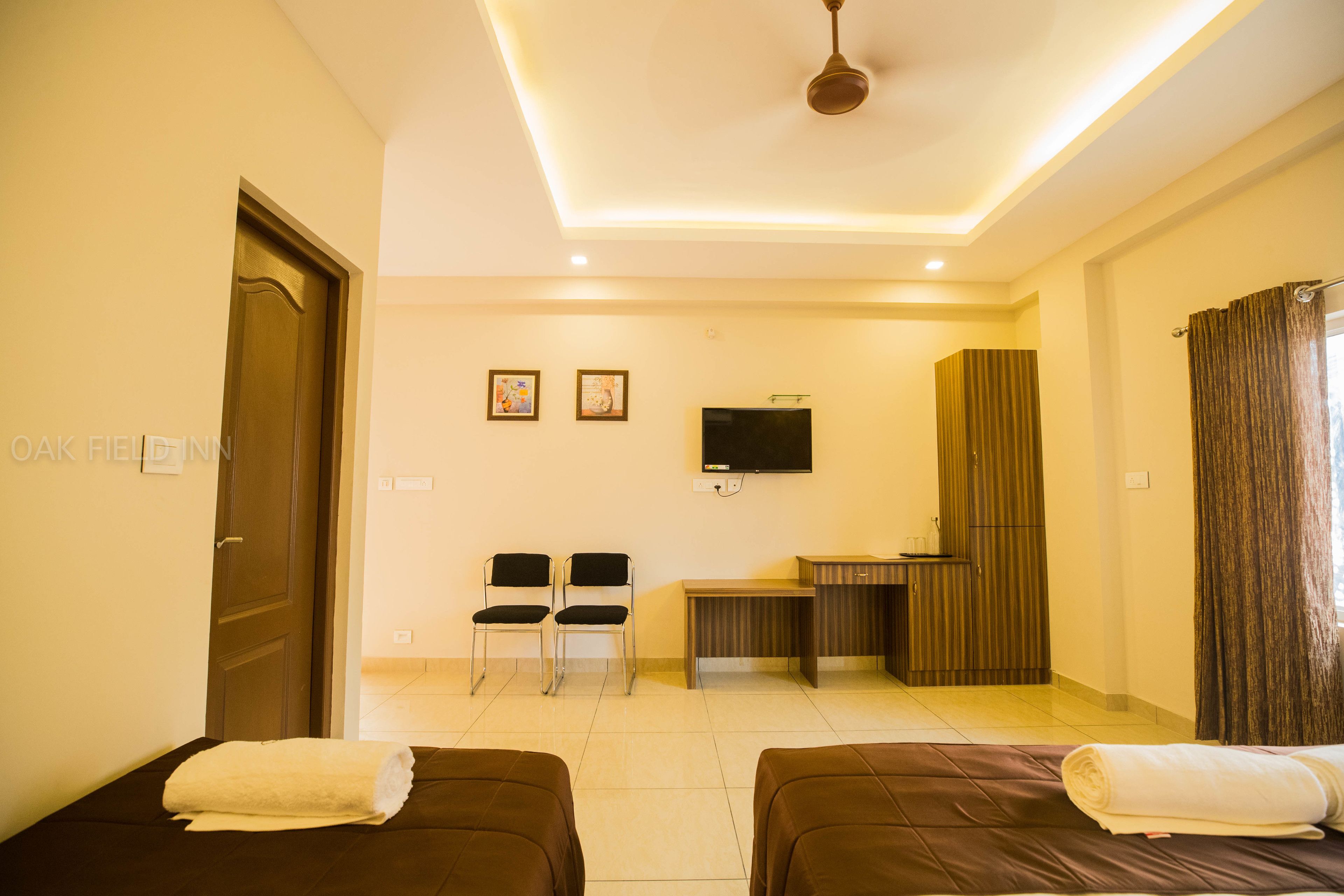 A hotel room with two beds, a desk, a TV, and a shower area.
