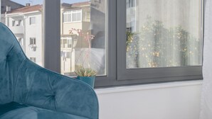 A room with a blue sofa, a potted plant, and a window with a view of neighboring buildings. - Liiiving | Bright Light Studio (Porto)