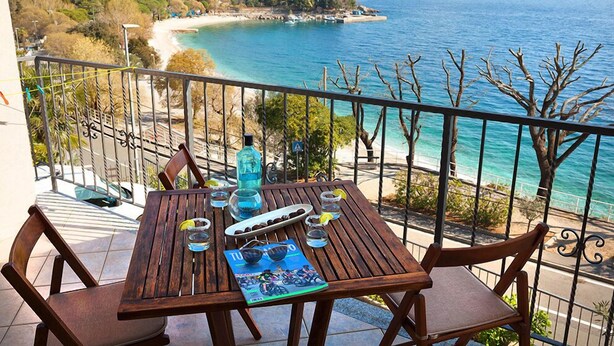 A wooden table with chairs on a balcony overlooking a beach and the sea. - Villa Lidija (Lovran)