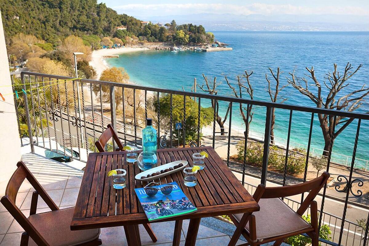 A wooden table with chairs on a balcony overlooking a beach and the sea.